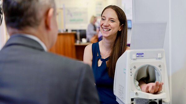 Emma Holland-Lindsay at a GP practice with her arm in a machine while talking to a man in a suit.